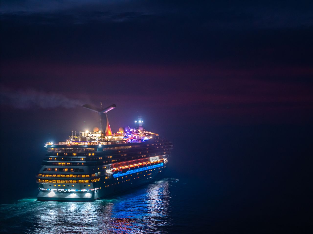 mobile-02 A brightly lit cruise ship sails through the ocean under a vivid night sky.