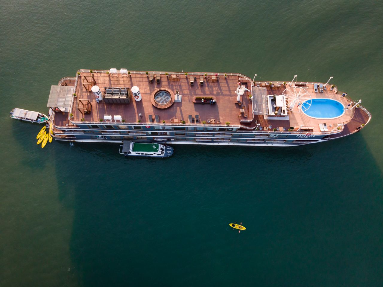 creative-02 Drone shot capturing a luxurious cruise ship sailing in clear waters, complete with a pool and kayaks.